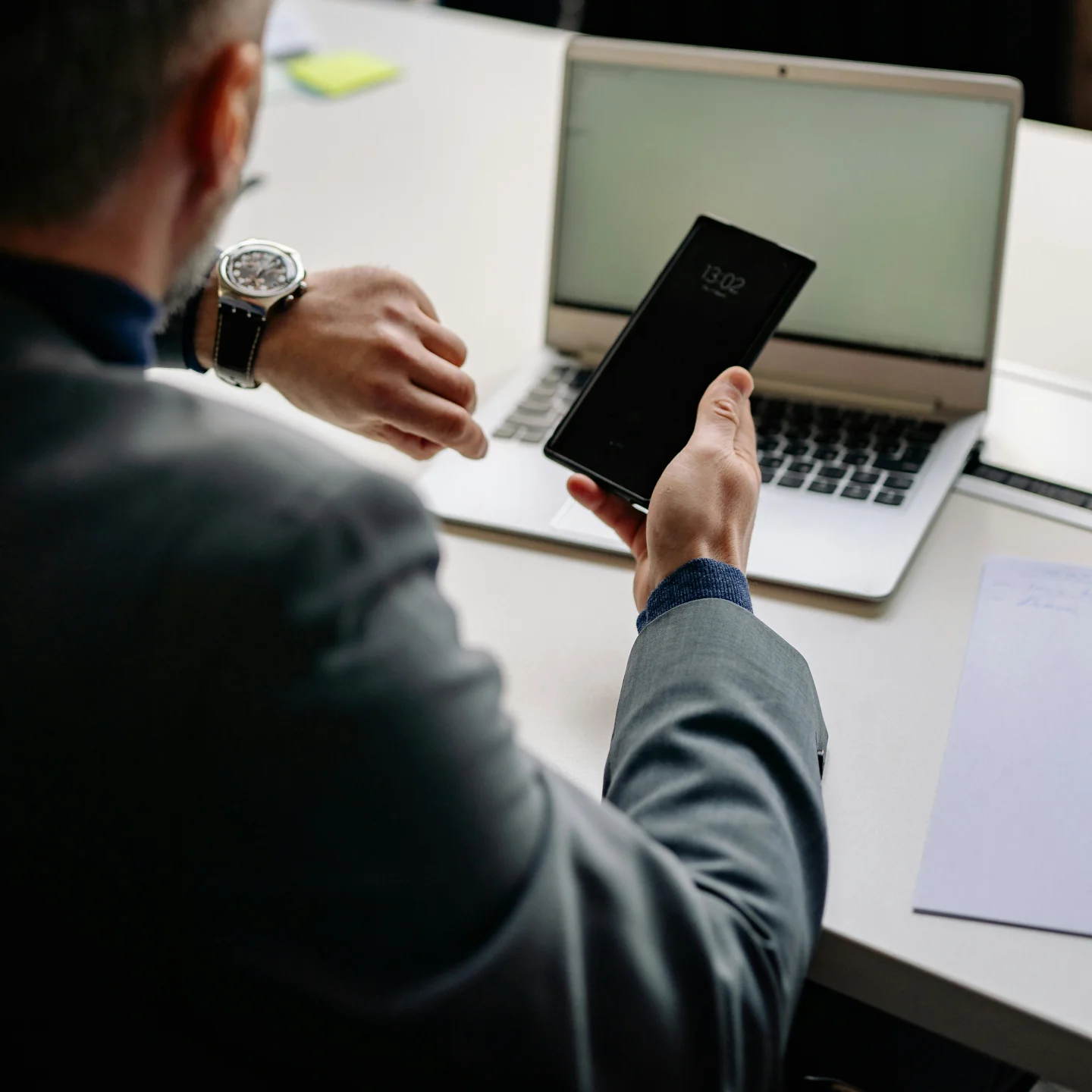 A businessman sitting behind a desk in a modern office looking at a watch
